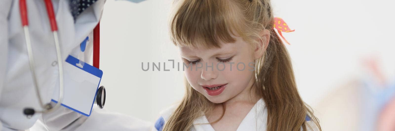 Doctor pediatrician in protective medical mask talking to little girl patient in clinic. Treatment of covid19 in children concept