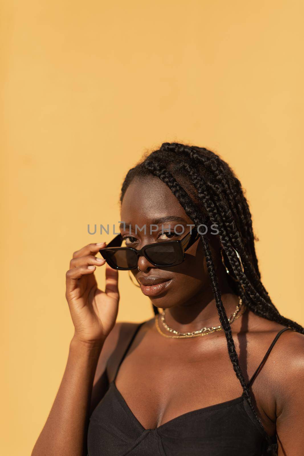 Close-up portrait of a young black woman looking at camera with expressive gaze over glasses during sunset