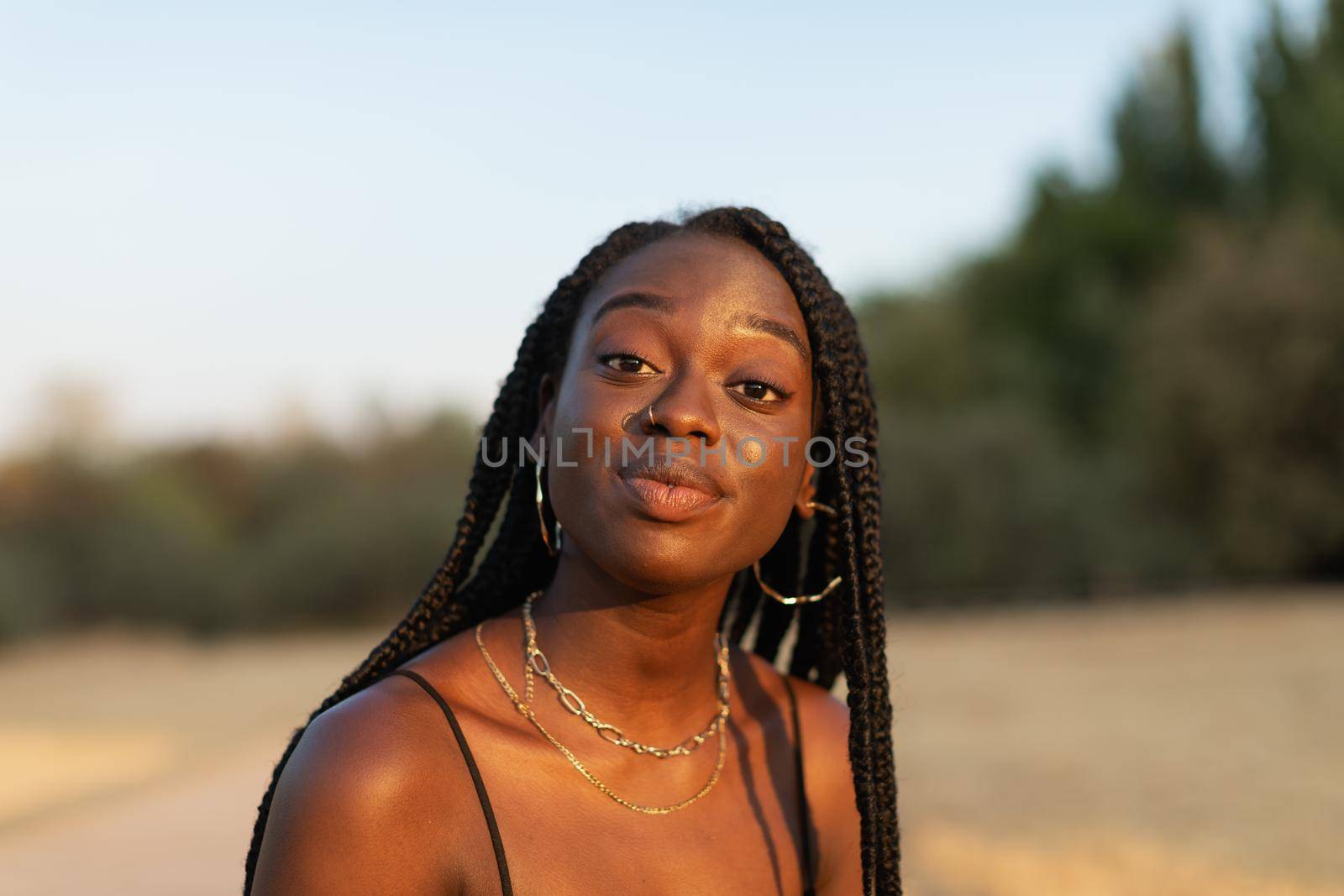 Close-up portrait of a young black female expressively looking at camera in the park by stockrojoverdeyazul