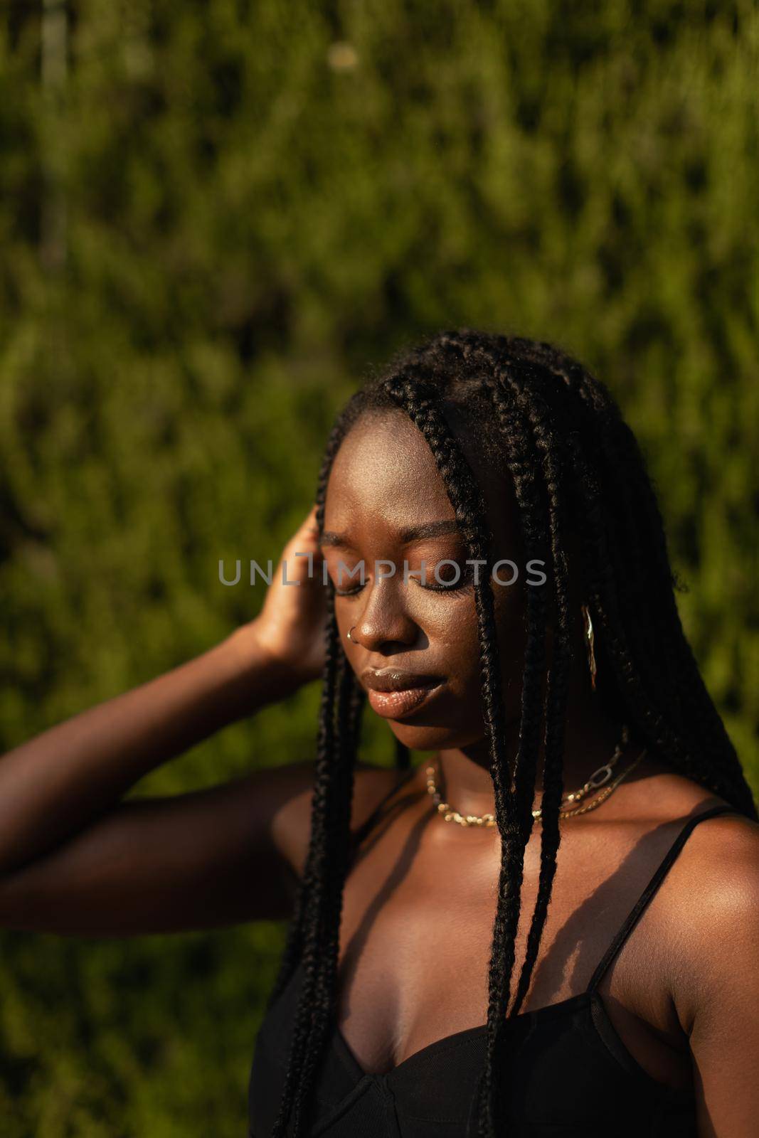 Portrait of a young black female removing her hair from her face whit her eyes closed by stockrojoverdeyazul