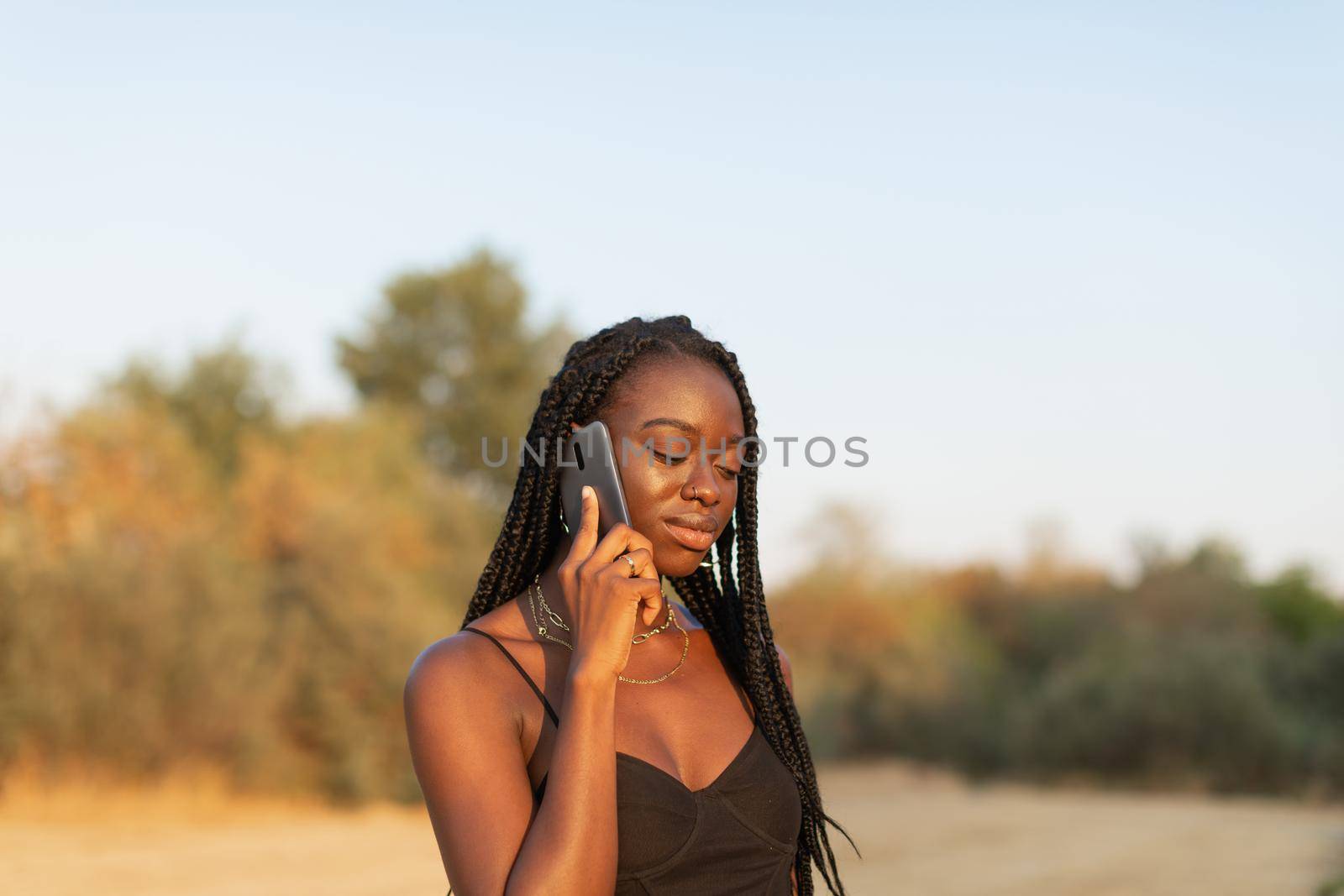 Young black female talking on the phone in the park by stockrojoverdeyazul
