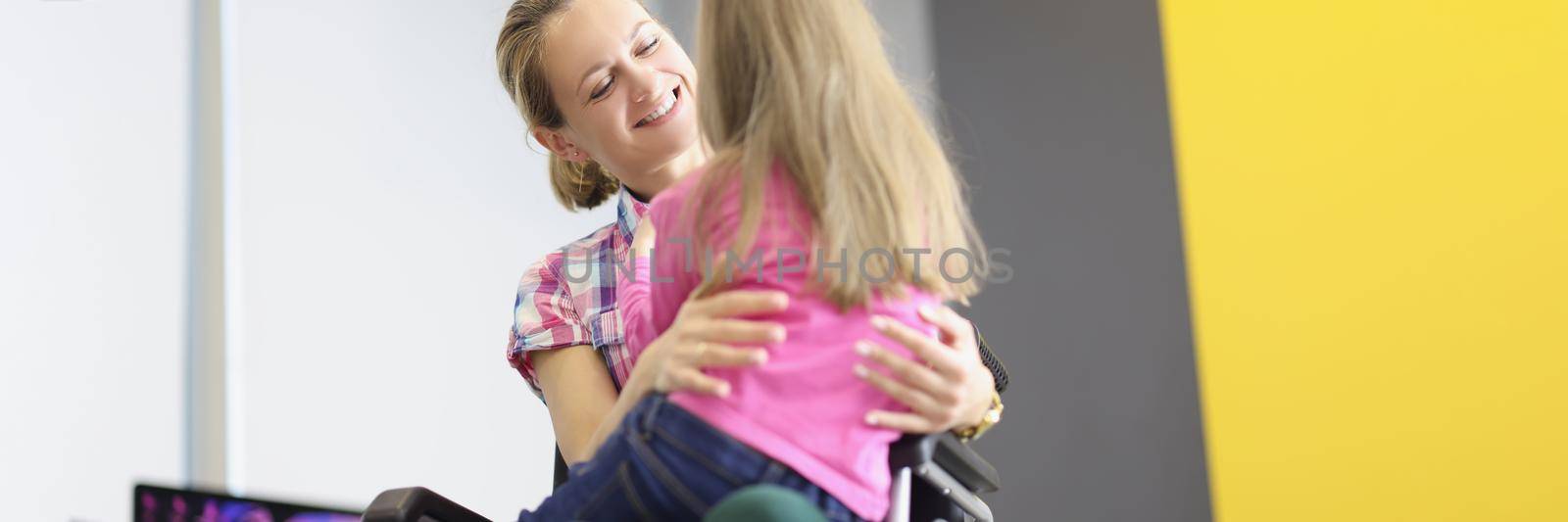 Young woman sitting in wheelchair and hugging her little daughter. Full life of disabled people concept