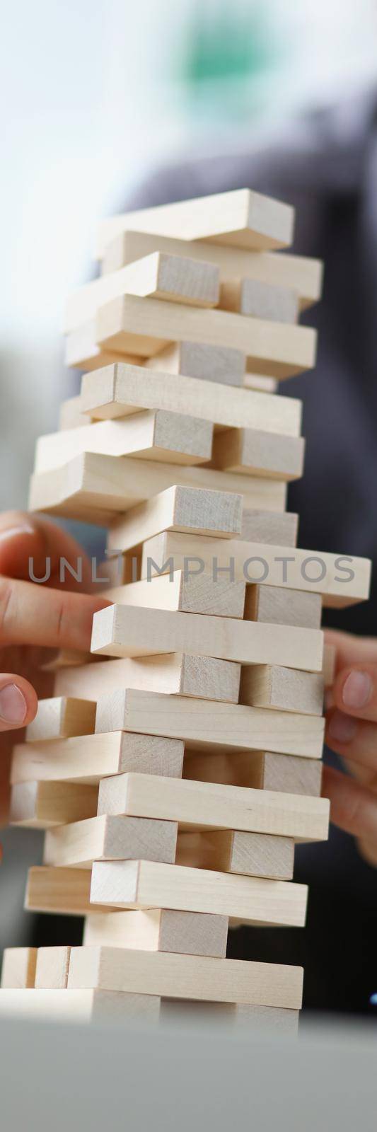 Young man removing wooden blocks from toy tower closeup. Board games concept