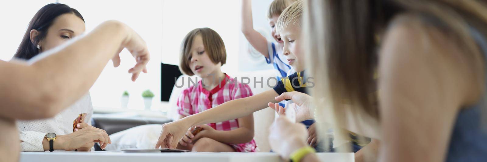 Adults and children playing board games at table at home by kuprevich