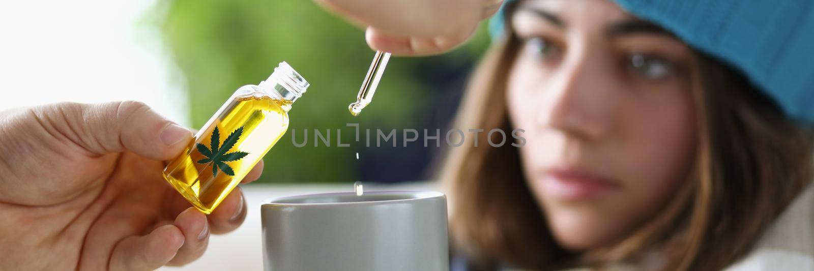 Drops of marijuana oil dripping into cup of sick woman wearing hat closeup. Cannabis addiction concept