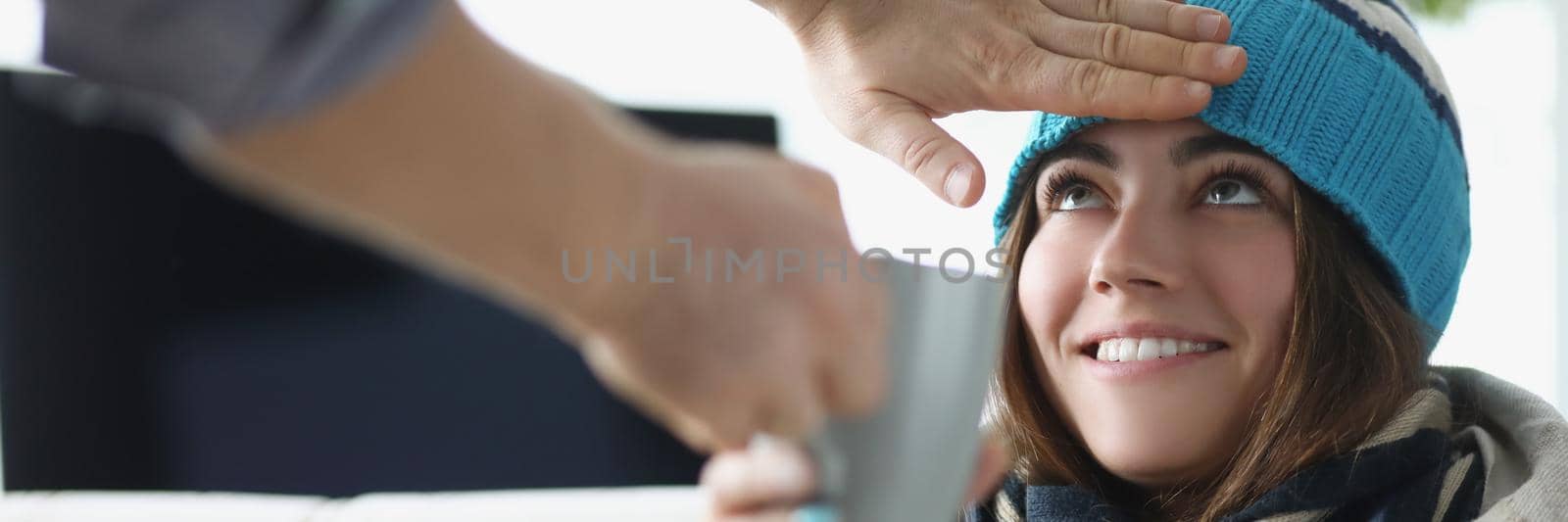 Man hand touching forehead of sick woman in hat and giving cup of tea by kuprevich