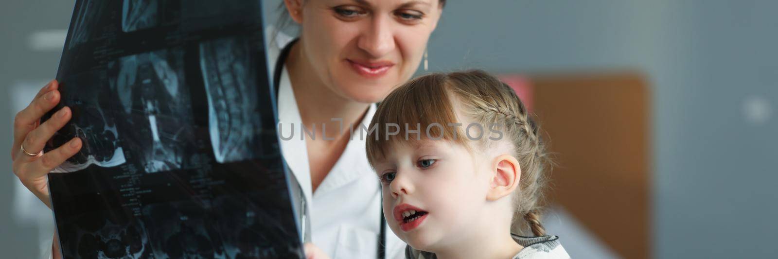 Woman doctor showing little girl xray in clinic. X ray diagnostics in pediatrics concept