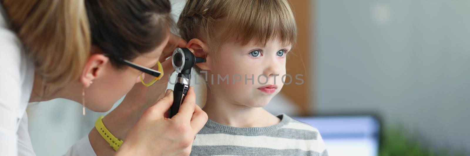 Female pediatrician looking at ear of little girl using otoscope in clinic. Hearing loss diagnosis in children concept