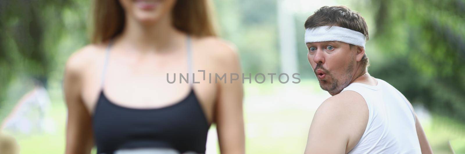 Fat man looking at young woman athlete jogging in park. Morning jogging healthy lifestyle concept