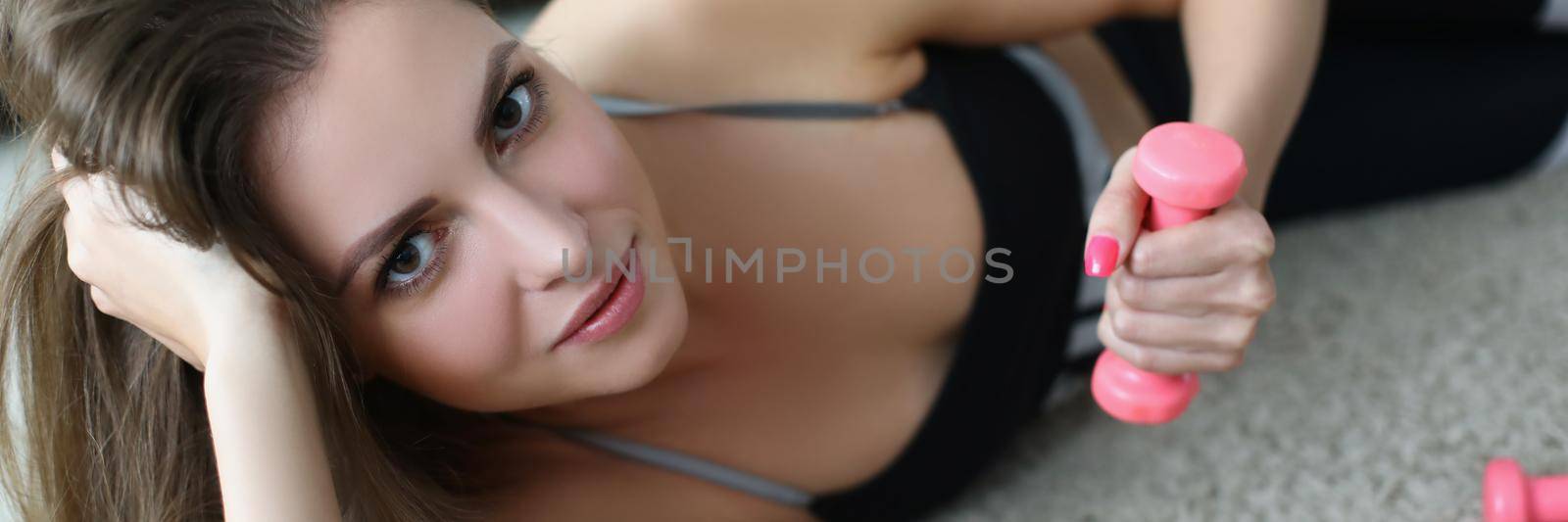 Young woman with pink dumbbells in her hands lying on floor at home by kuprevich