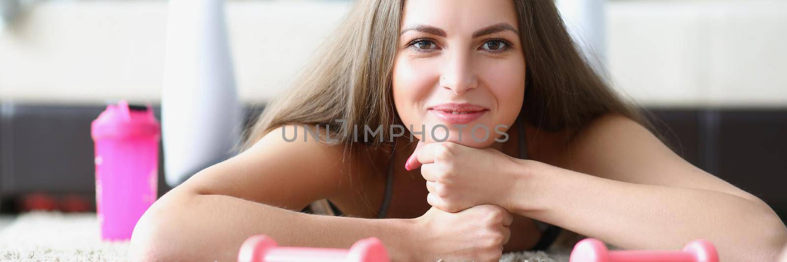 Young woman athlete with dumbbells in her hands lying on floor at home by kuprevich