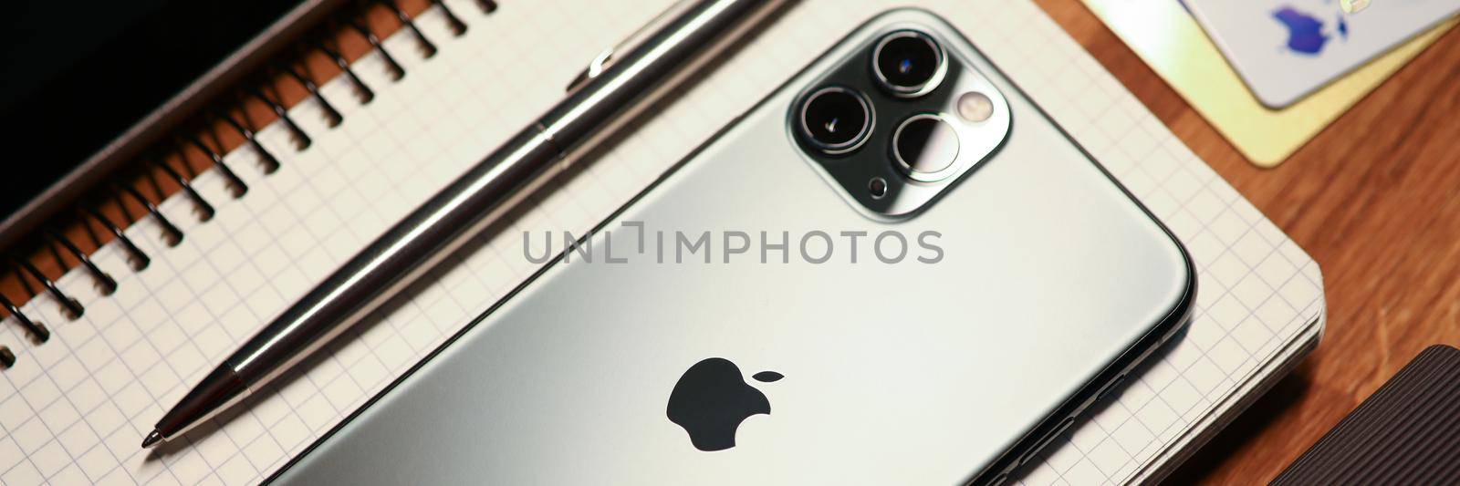 Minsk, Belarus - December 11, 2019: new mobile phone iphone 13 pro lying on notebook with pen closeup. Payment of utility bills remotely via Internet concept