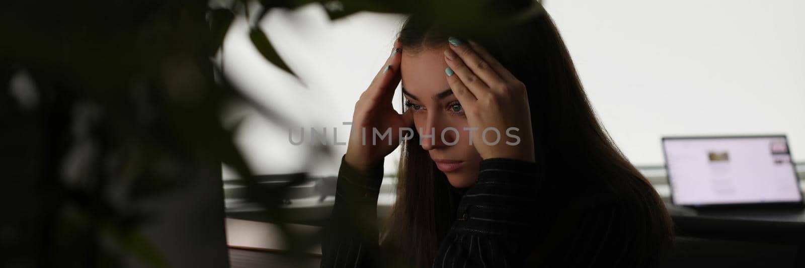 Tired woman holding her head with hands in front of computer screen in office by kuprevich