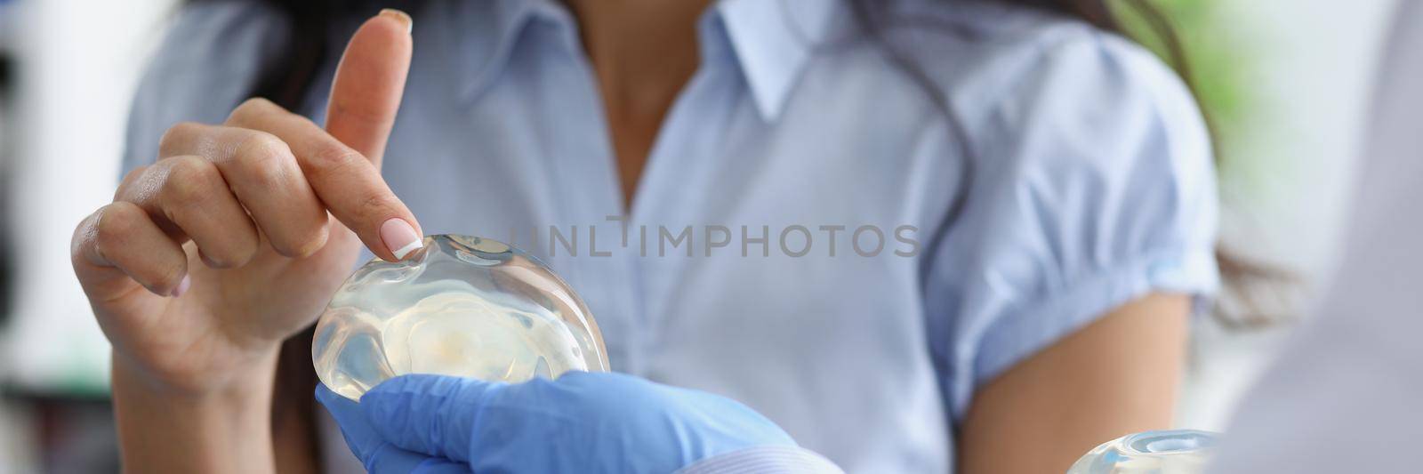 Female patient touching silicone implant on doctor hand with her finger closeup by kuprevich