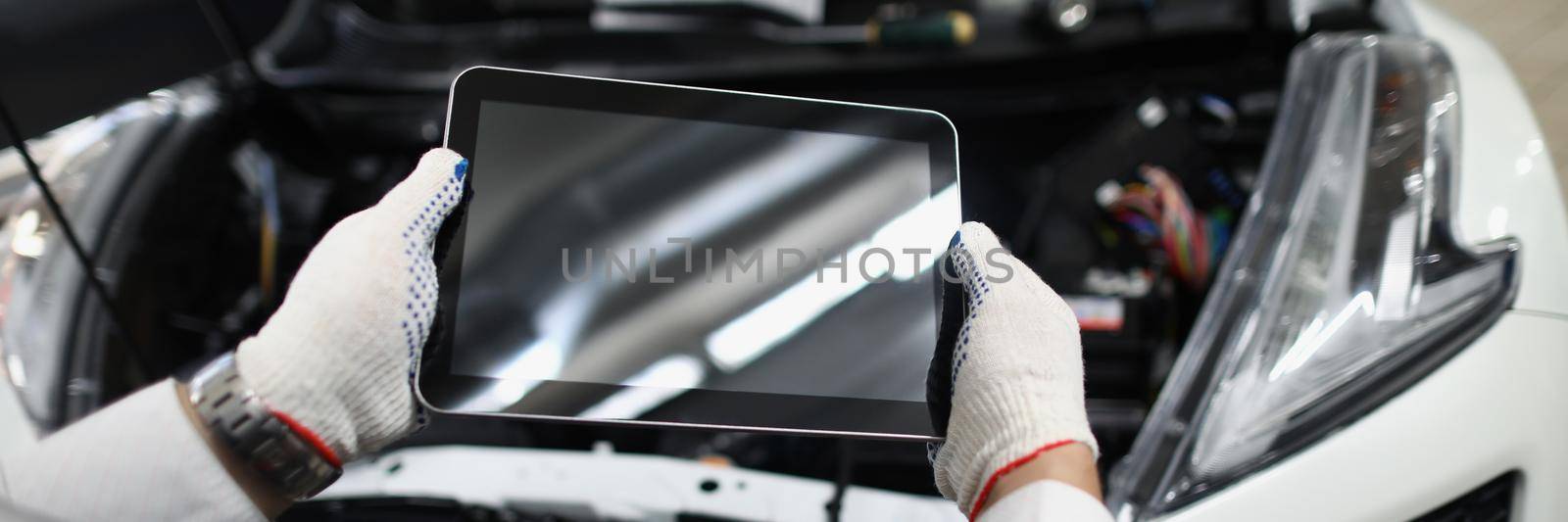 Master repairman holding digital tablet near open hood of car closeup by kuprevich