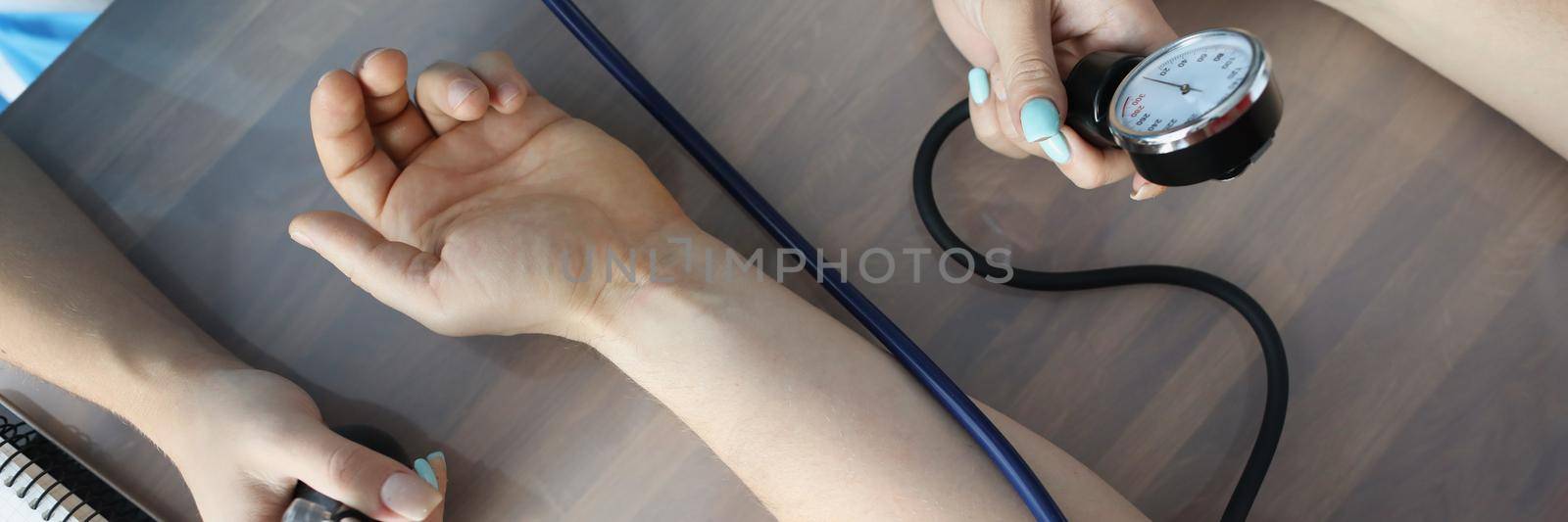 Doctor measuring blood pressure with tonometer at table in clinic closeup by kuprevich