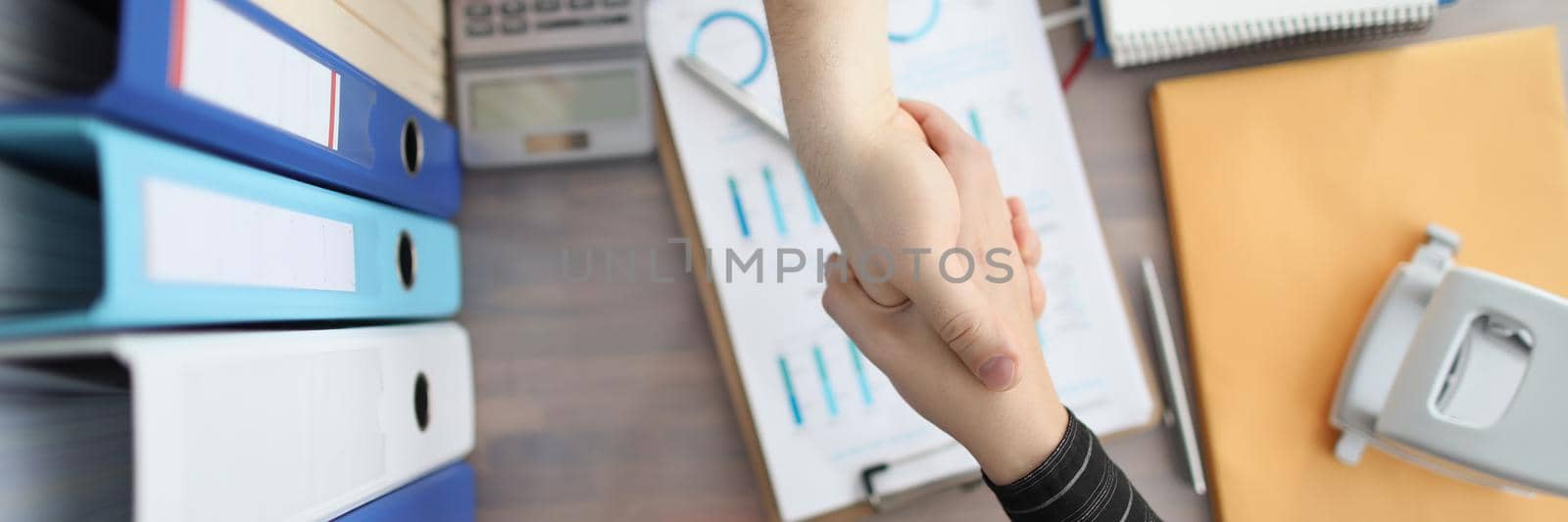 Closeup of handshake of business people on background of documents and folders on table top view. Successful partnership work in business concept