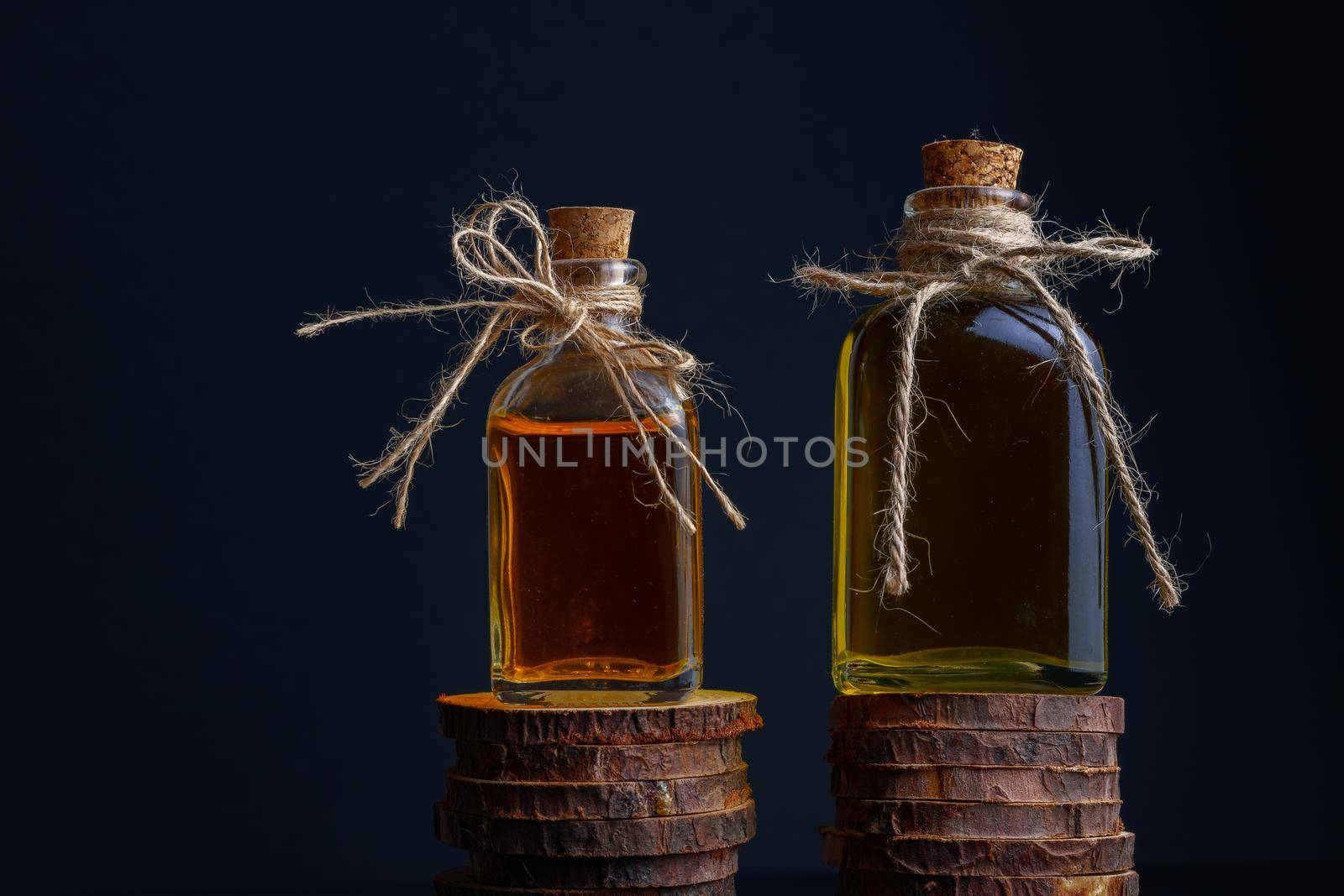 close-up of two glass bottles with cork stopper and raffia string with rosemary oil and rose oil on a dark background