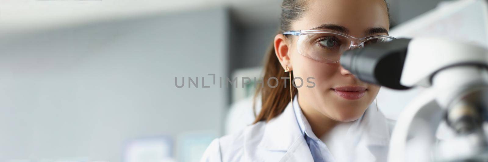 Woman scientist chemist looking through microscope in laboratory by kuprevich