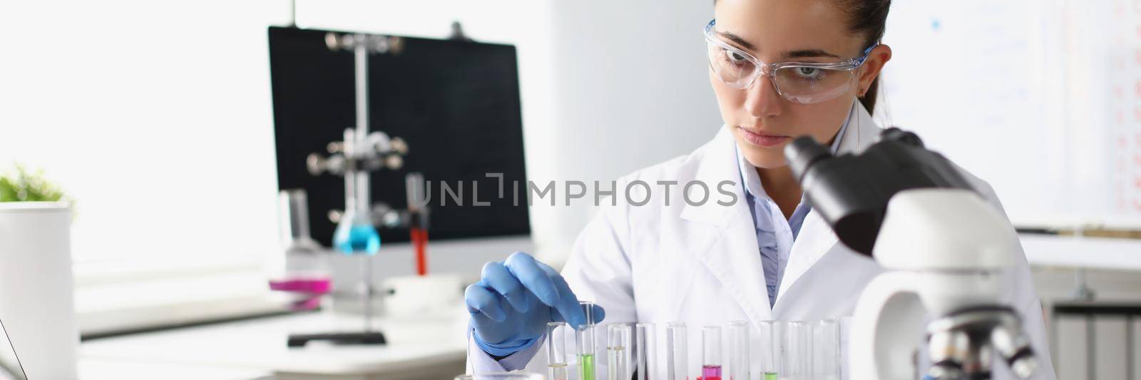 Chemist woman holding test tube with liquid in front of microscope in laboratory by kuprevich