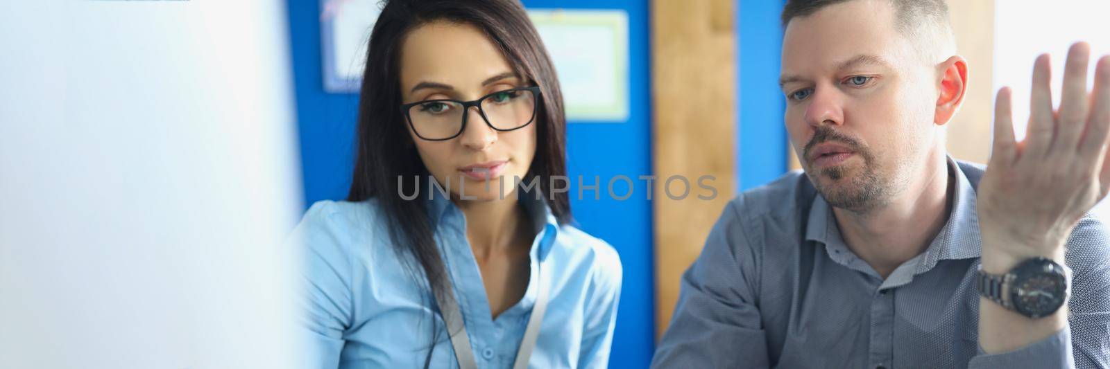 Man and woman in glasses sitting at table in front of computer screen by kuprevich