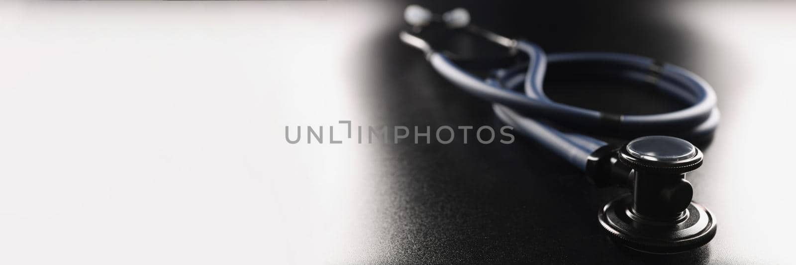 Dark blue stethoscope lying on black background closeup by kuprevich