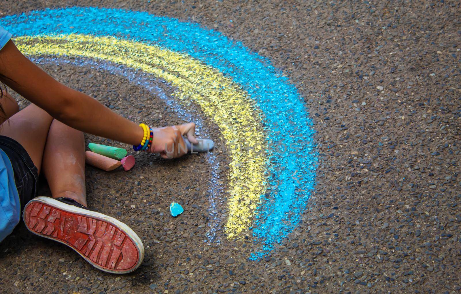 A child draws a rainbow on the asphalt. Selective focus. by mila1784