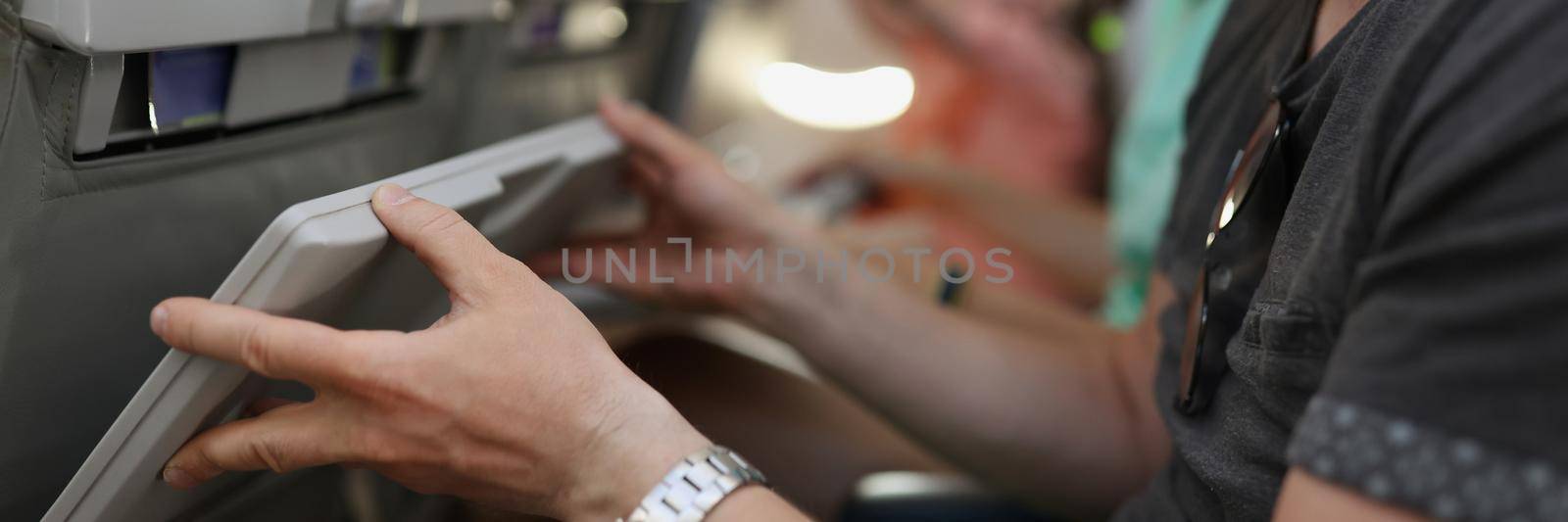 Man in protective medical mask lifting table on airplane seat closeup. Rules of conduct on airplane during pandemic covid19 concept