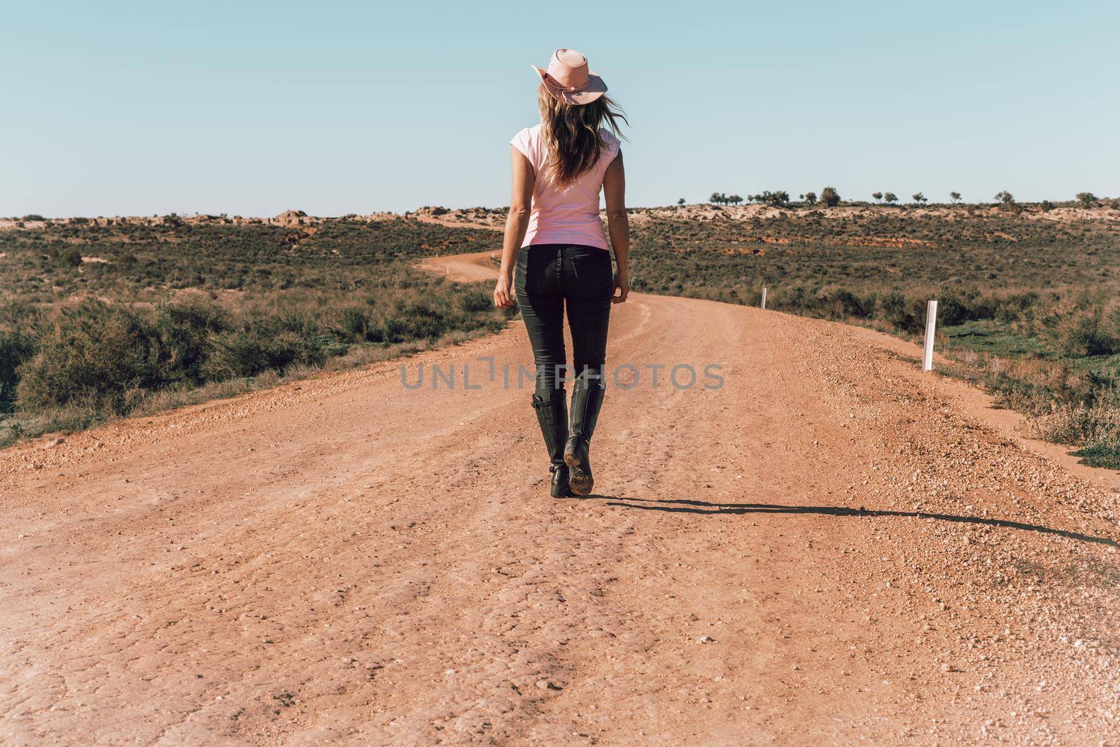 A woman wearing jeans and t-shirt walking dusty roads of outback Australia