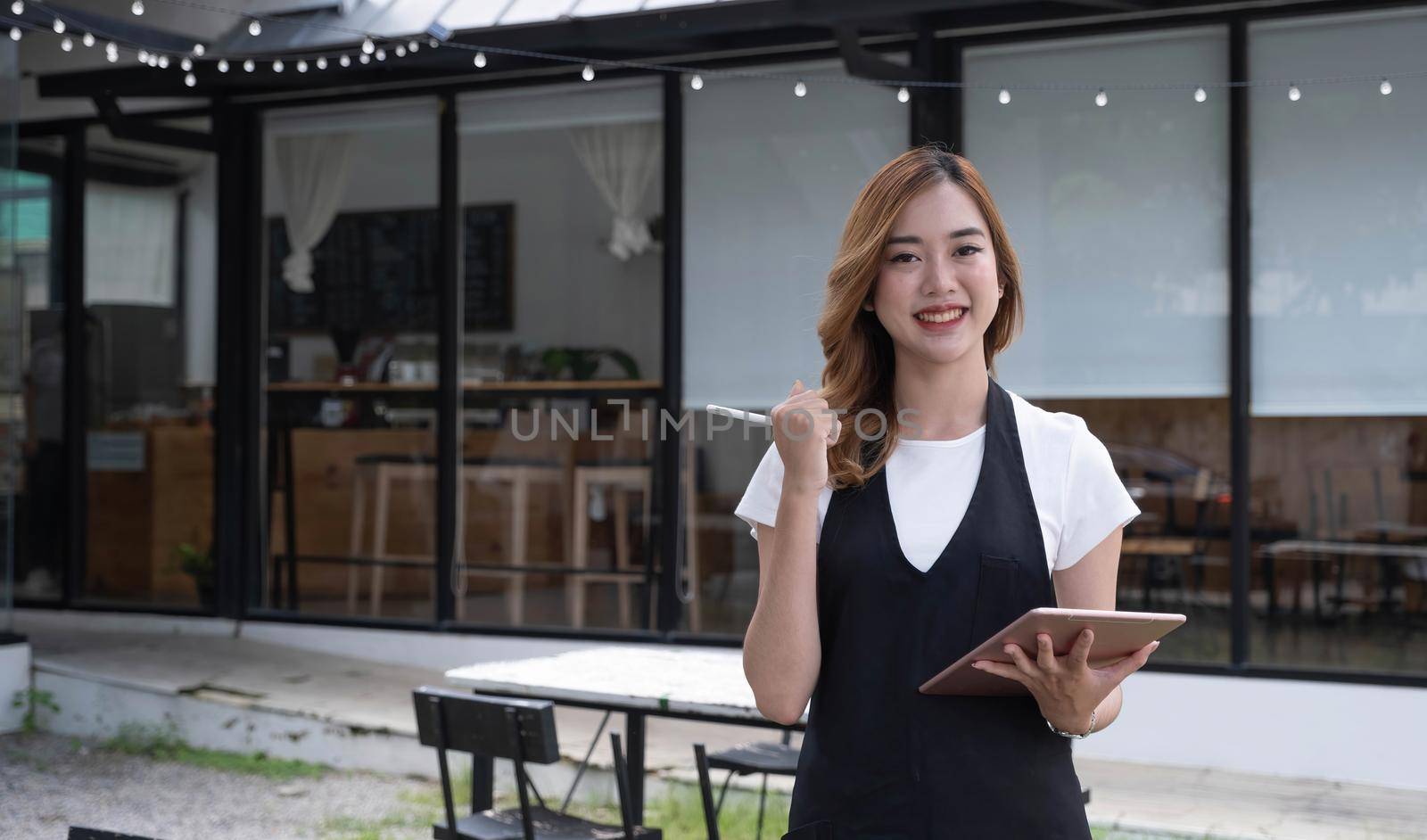 Attractive beautiful young Asian female restaurant or coffee shop waitress noting a customer's order on a digital tablet. by wichayada