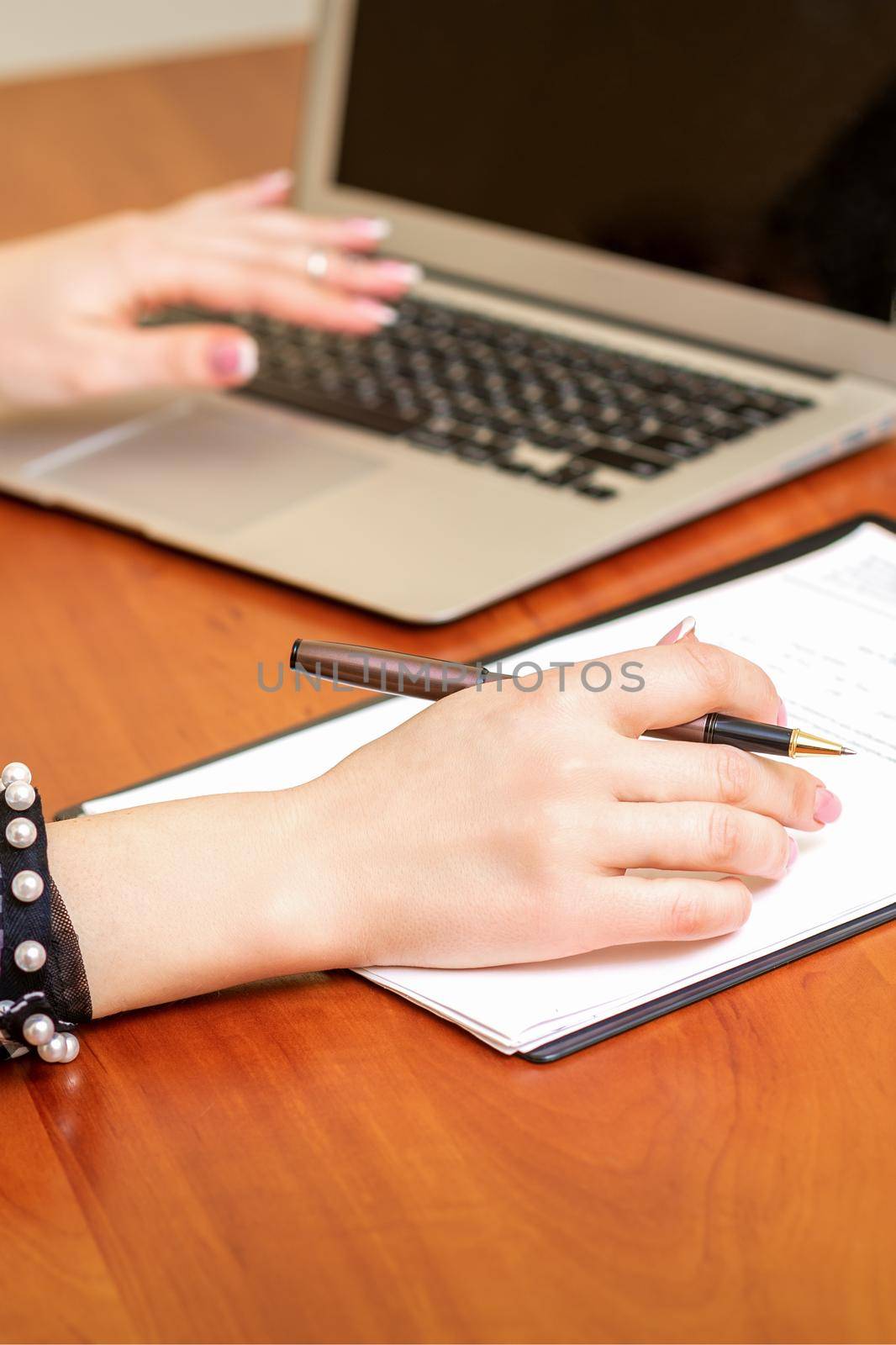 Female hands holding pen under the document and working with laptop at the table in an office