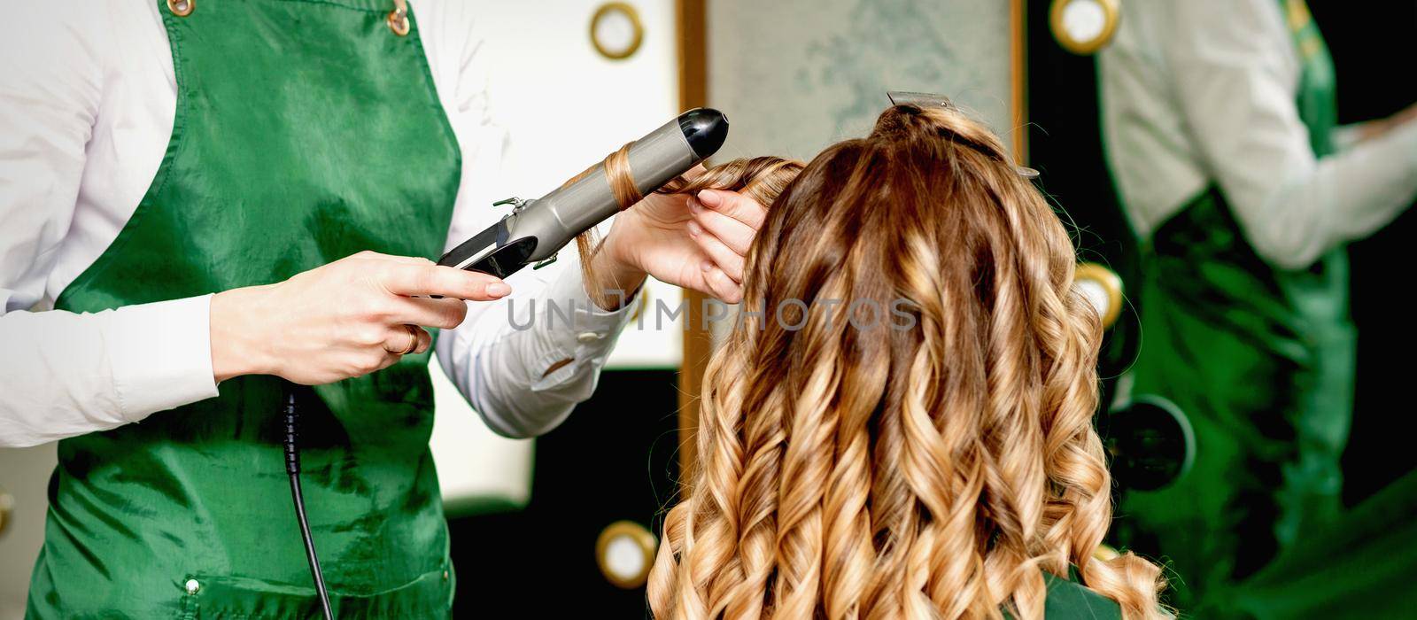 Hairdresser curling hair with curling iron by okskukuruza