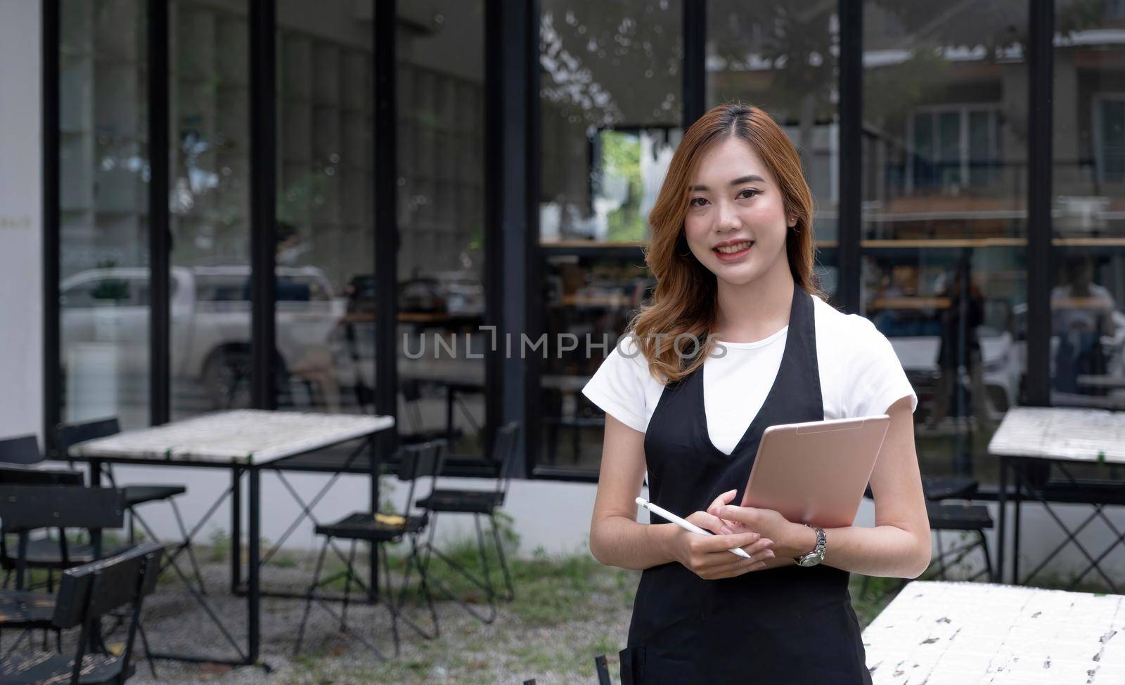 Portrait, Beautiful millennial Asian female waitress or restaurant owner standing in front of her restaurant entrance. Restaurant or coffee shop business owner concept. by wichayada