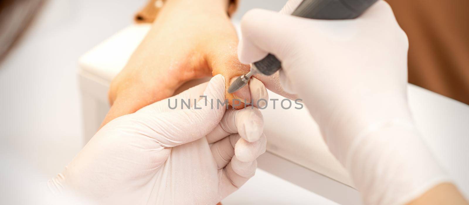 Manicure master applying electric nail file machine removing old nail polish on fingernails in a nail salon