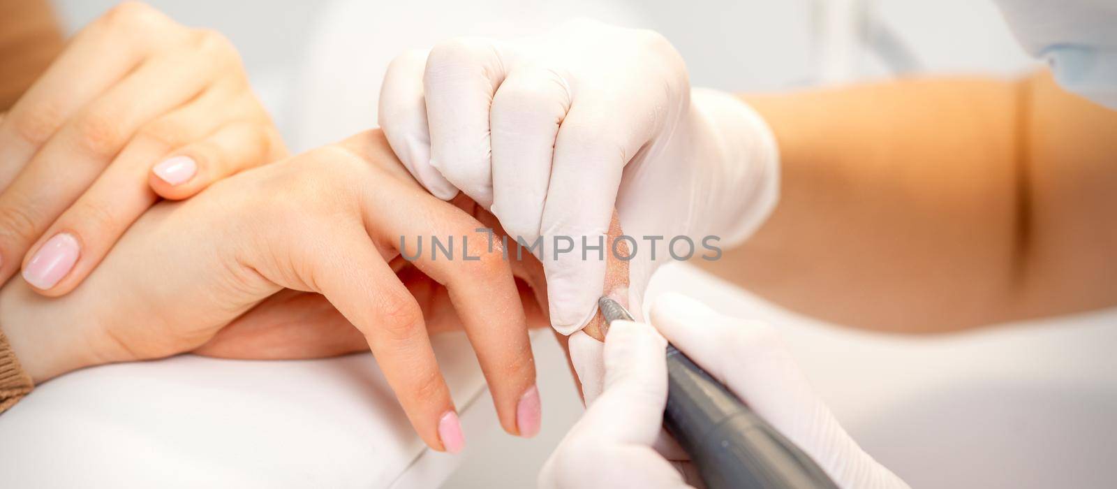 Manicure master applying electric nail file machine removing old nail polish on fingernails in a nail salon