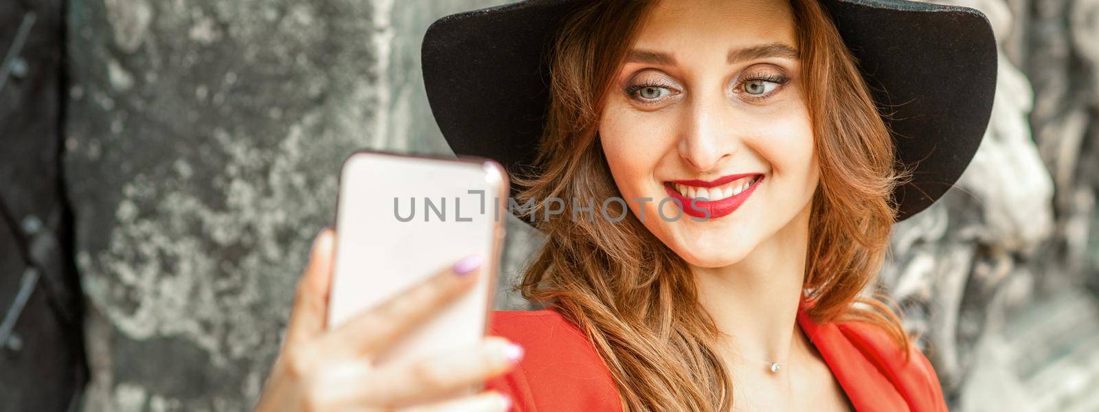 Close up of beautiful young caucasian woman taking selfie on smartphone standing and smiling against ancient building outdoors