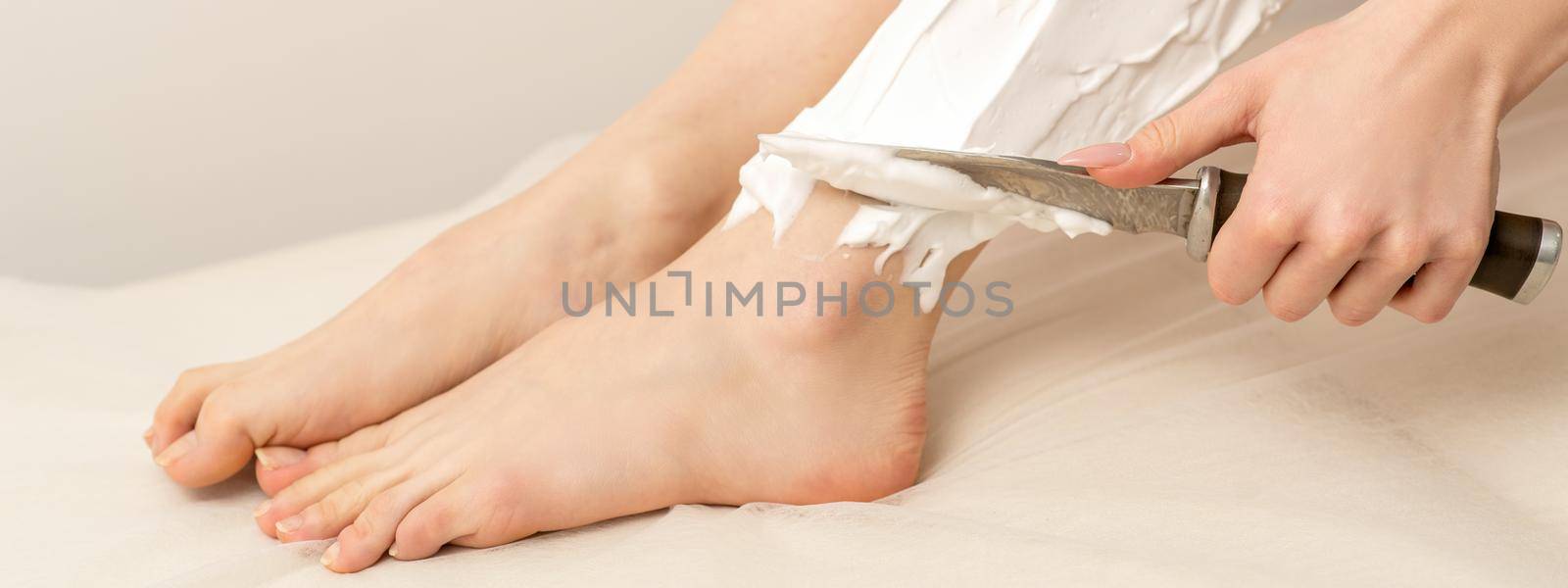 Beautiful young funny caucasian woman shaving legs with knife sitting on a white background