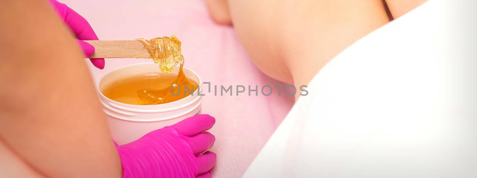 Cosmetologists waxing female legs with hot sugar paste in a beauty spa salon