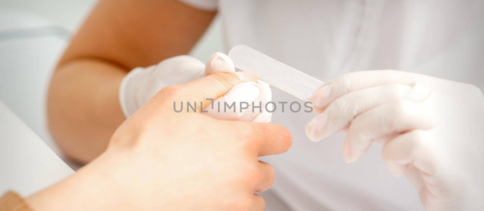 Close up of the hand of young woman receiving the nail file procedure in a beauty salon
