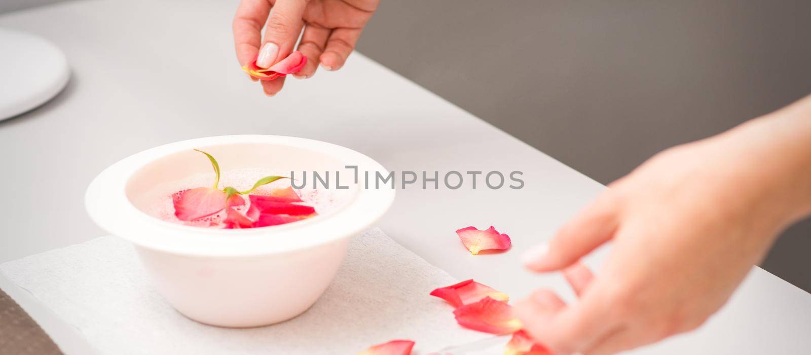 Beautician's female hands preparing manicure bath with red and pink roses petals on the table in spa