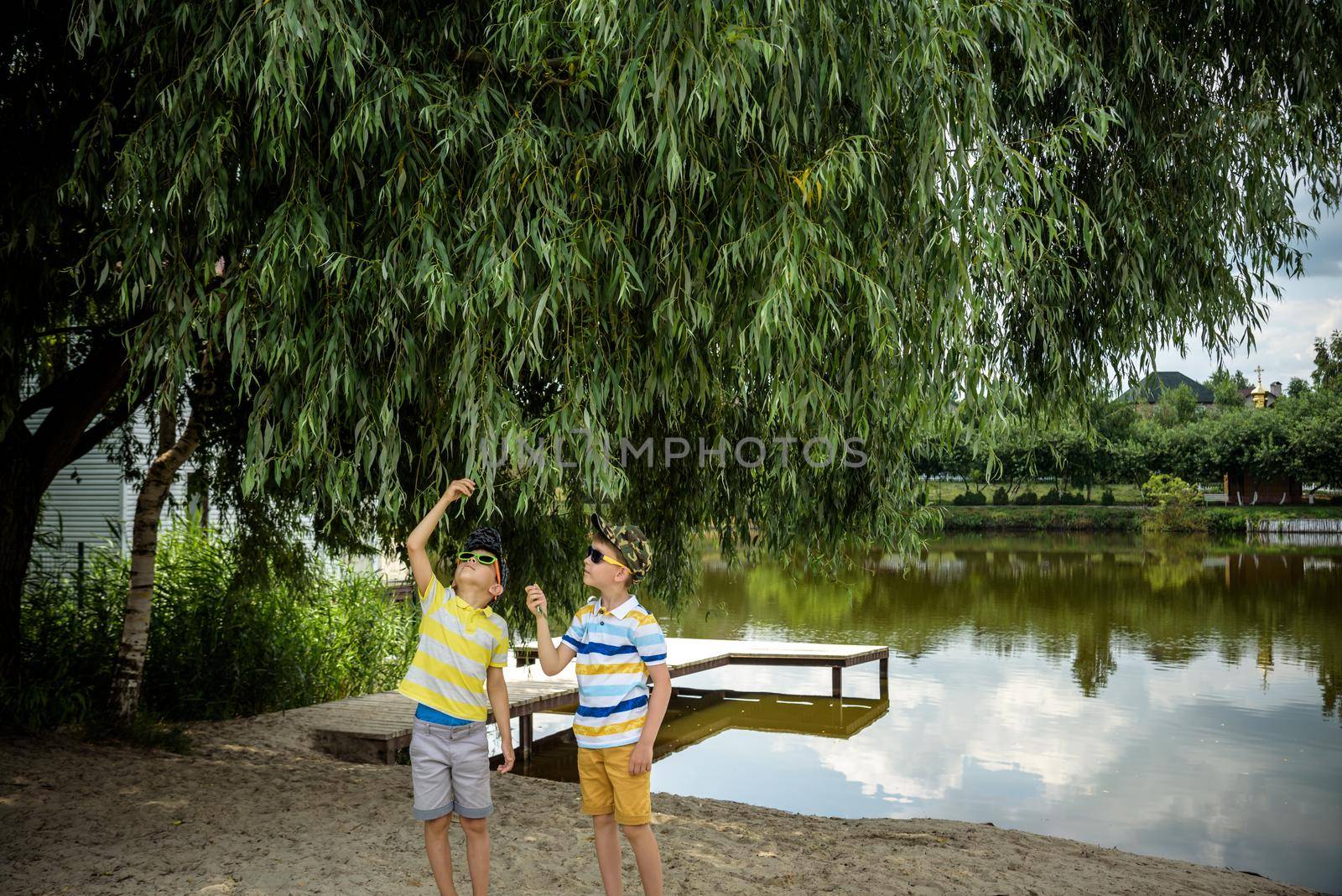 Siblings, brother, hugs. Two children, older boy and his younger brother standing on the shore of the lake near old tree. Summertime holiday concept leisure time on nature.