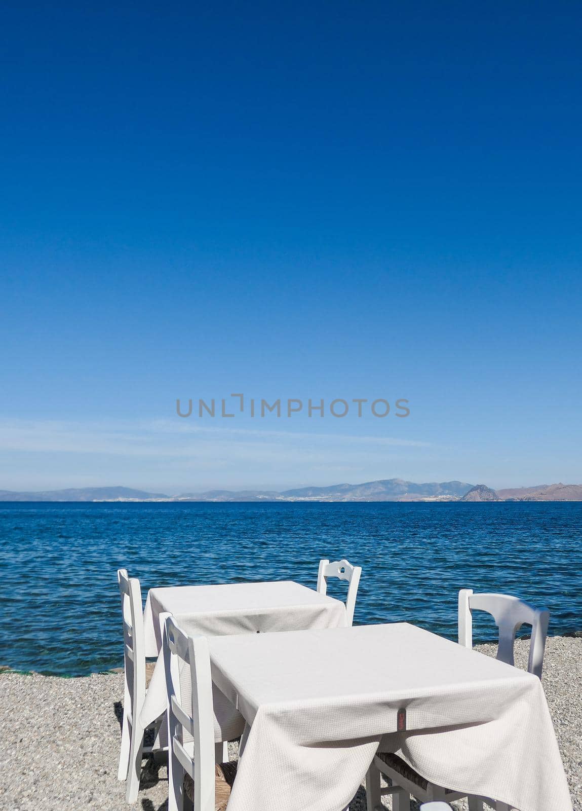 White restaurant tables on the beach in summer - travel, vacation and summer concept. The perfect lunch with a sea view