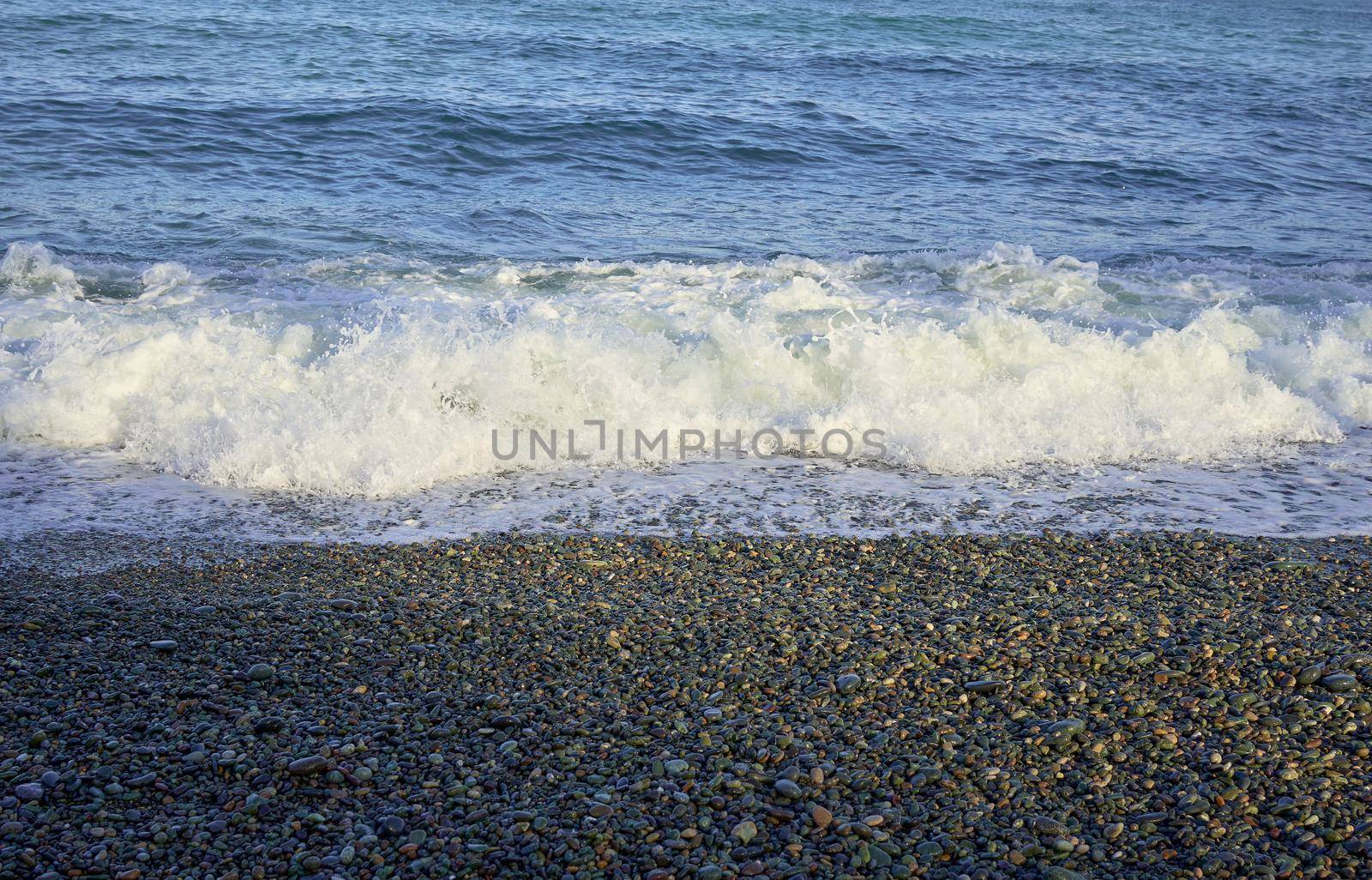 Sea shore with pebbles, wet sea pebbles on the beach and quiet sea surf. Restless sea and waves.