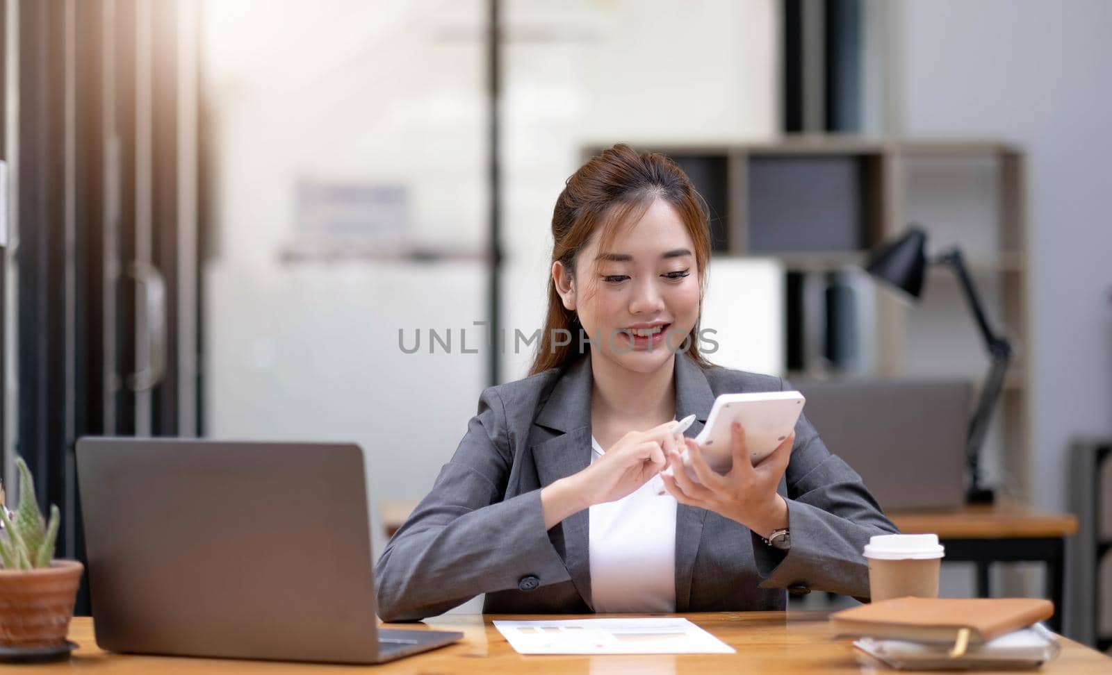 Young Asian businesswoman using a calculator to calculate business principles. Accounting statistics concept at the office..