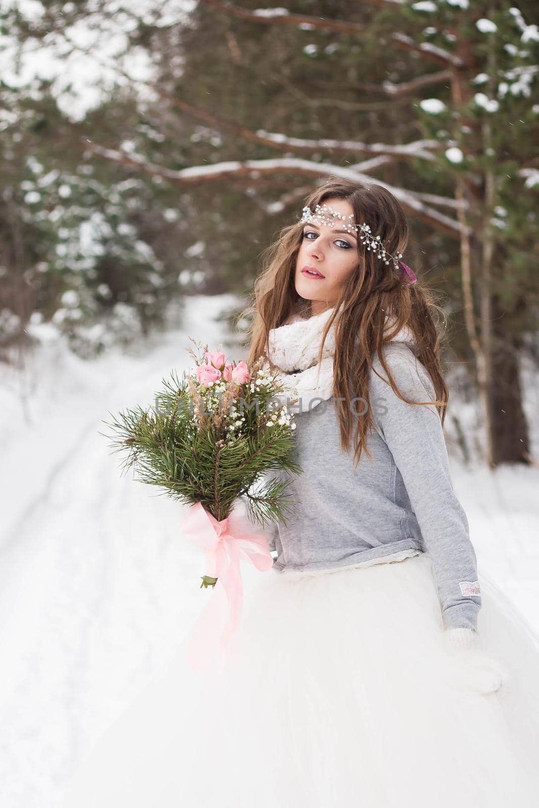 Beautiful bride in a white dress with a bouquet in a snow-covered winter forest. Portrait of the bride in nature.