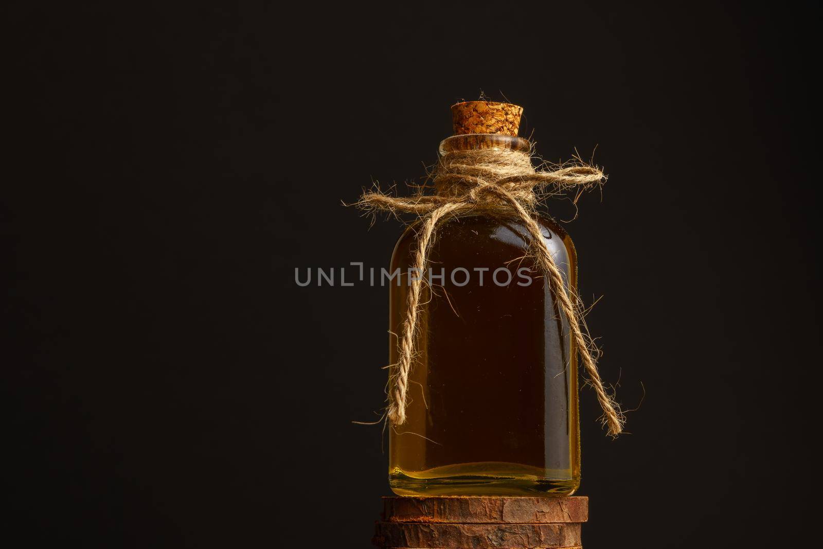 close-up of a glass bottle with cork stopper and raffia rope with rosemary oil on a dark background