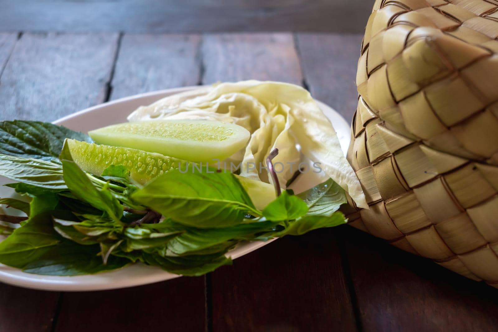 Bamboo wicker sticky rice basket called "Kratip" in the northeastern province, Thailand served with a vegetable side dish on the wooden table.