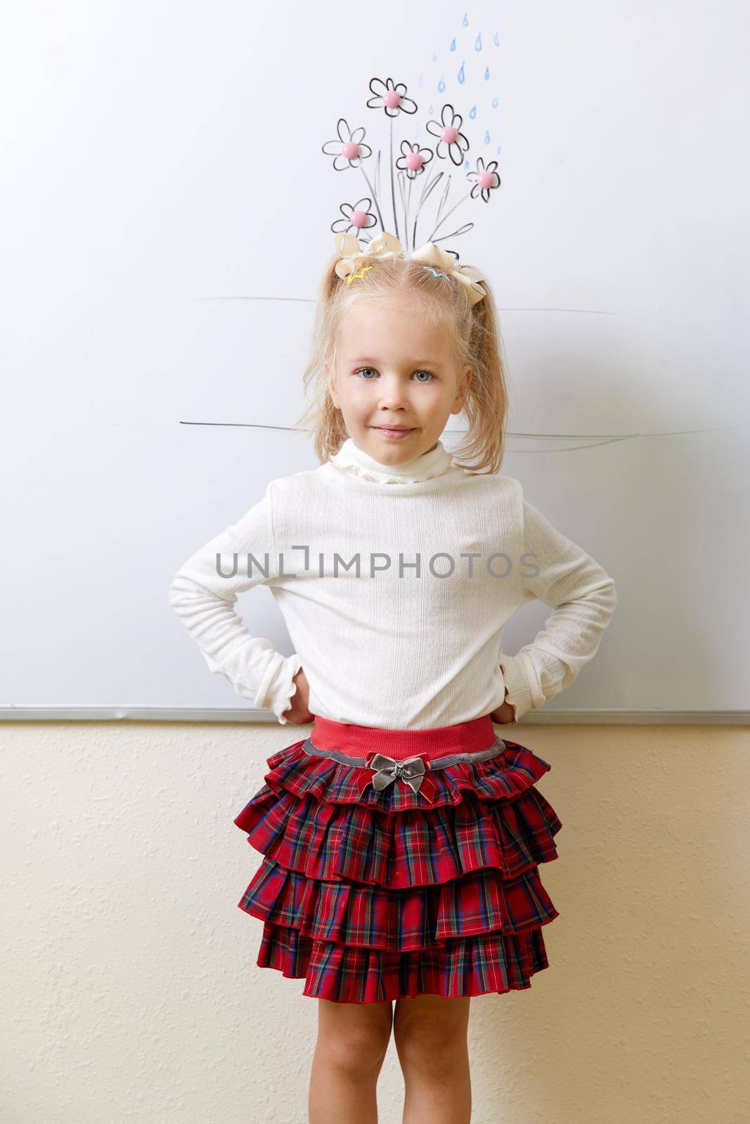 Little girl standing near white board in a class with flowers drawing on board