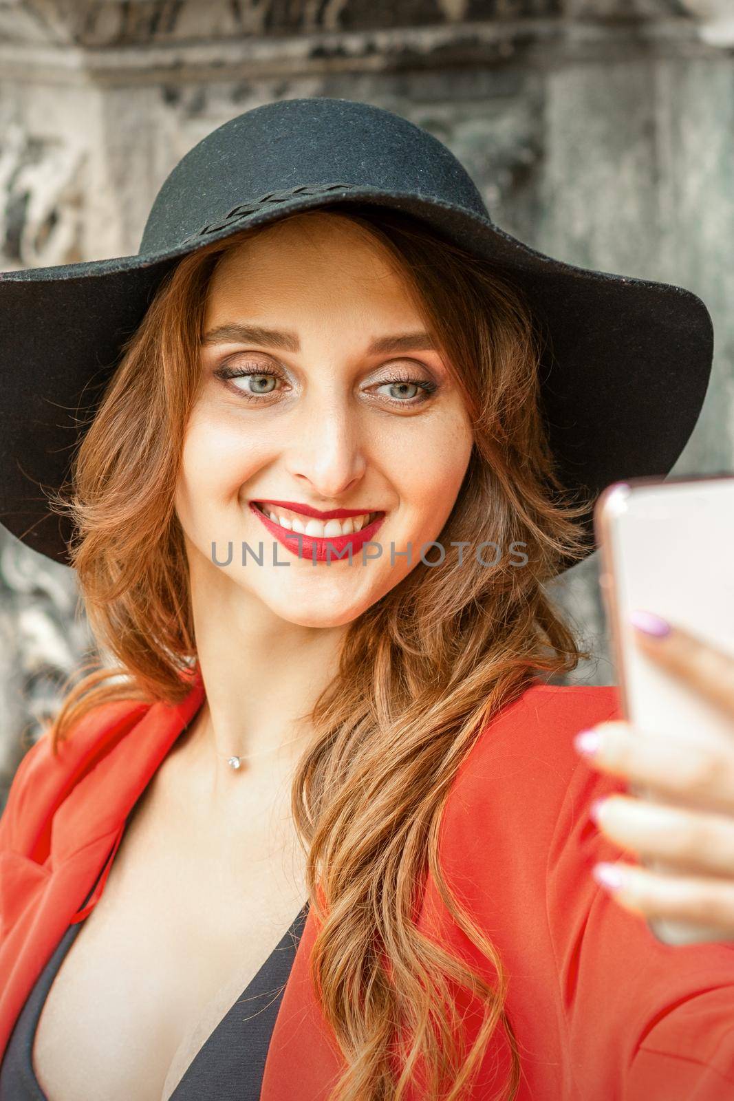 Close up of beautiful young caucasian woman taking selfie on smartphone standing and smiling against ancient building outdoors