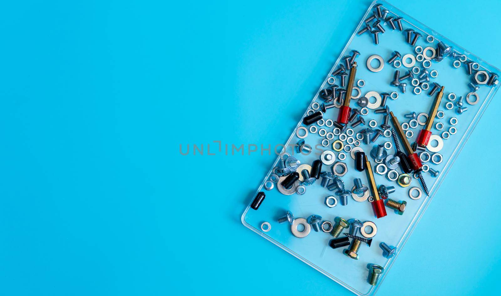 Top view metal bolts, nuts, washer, and screw in a plastic tray on blue background. Fasteners equipment. Hardware tools of mechanics technicians. Threaded fastener accessories. Hardware nuts and bolts